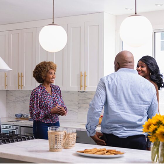 Group of people having a conversation in a kitchen setting.