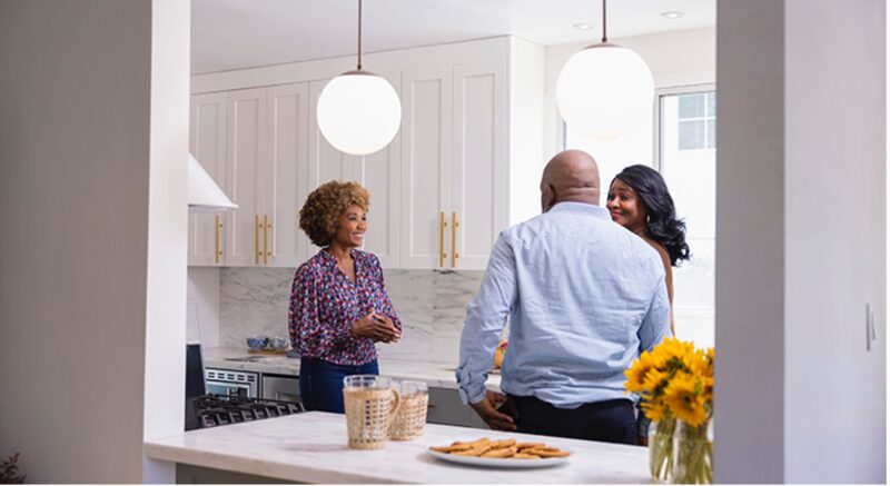 Group of people having a conversation in a kitchen setting.